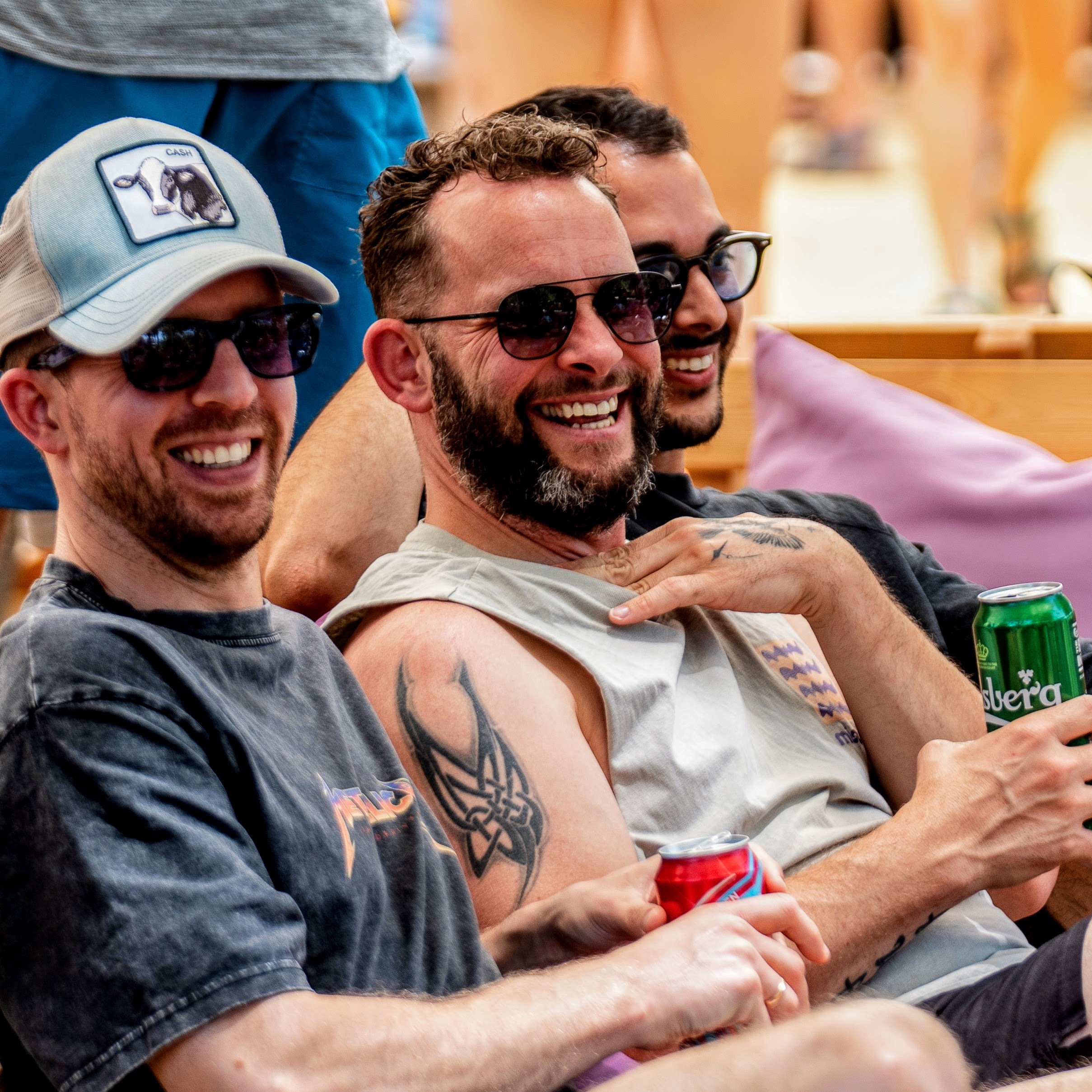 Three men in sunglasses sitting in a row, looking at something to the right and laughing